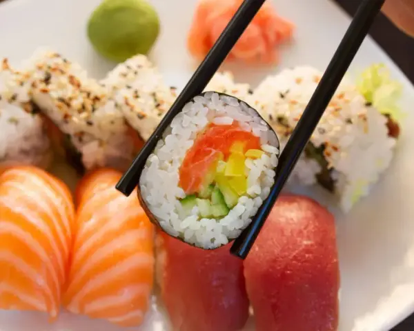 Pyszna rolka sushi z łososiem, ogórkiem i papryką, trzymana pałeczkami. Zastanawiasz się, ile waży rolka sushi?