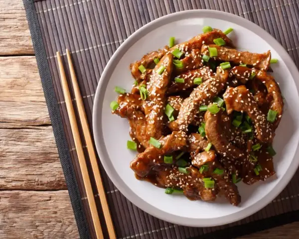 Pyszne kawałki wołowiny w sosie teriyaki, posypane sezamem i szczypiorkiem, gotowe do podania z pałeczkami.