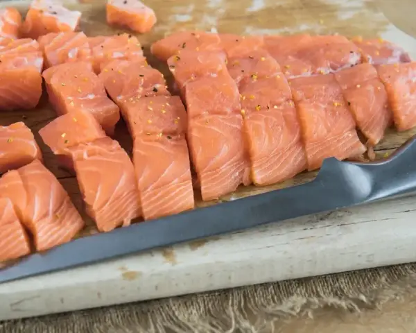 Pokrojona w kostkę i plastry świeża ryba do sushi, przyprawiona, leży na desce obok noża.