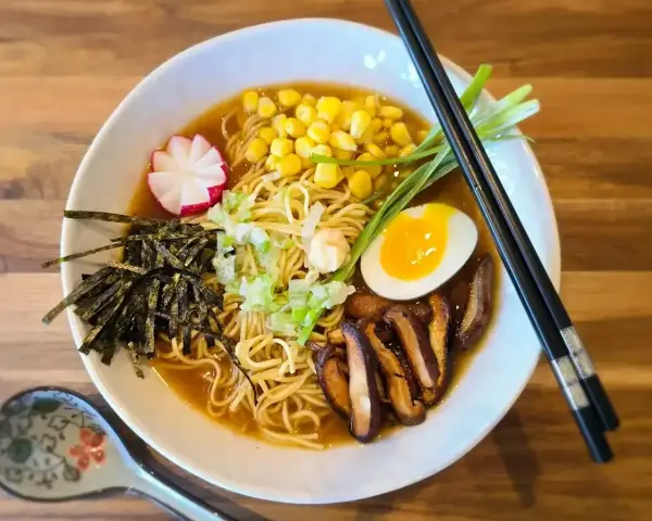 A miska pełna aromatycznego ramen miso z makaronem, jajkiem na pół, kukurydzą, grzybami shiitake, nori i szczypiorkiem.
