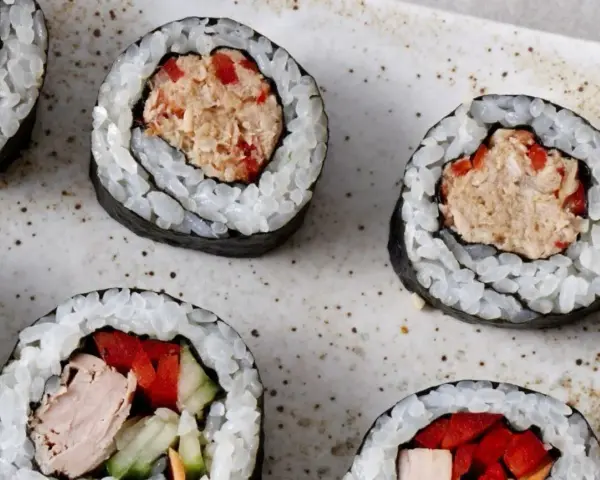 Kilka kawałków sushi z tuńczykiem i warzywami na talerzu.