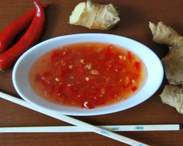 Ostry sos tao tao z kawałkami chili i imbirem, obok pałeczki i papryczki.