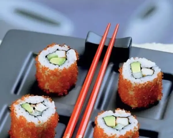 Cztery rolki sushi z awokado i rybą, obtoczone pomarańczową ikrą. Idealne sushi na diecie, podane z czerwonymi pałeczkami.