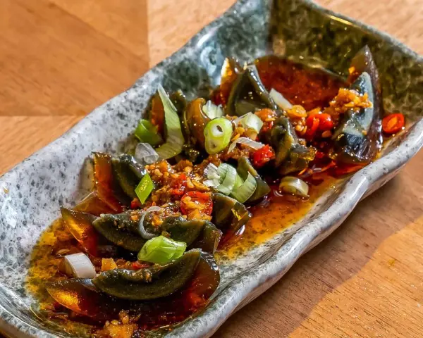 Kawałki 100 letniego jajka w pikantnym sosie z czosnkiem, chili i szczypiorkiem na kamiennej tacy.