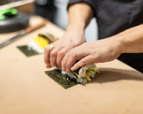 Dłonie zwijają sushi na arkuszu nori, ukazując jego wszechstronne właściwości kulinarne.