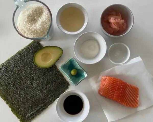 Wszystkie składniki do sushi: ryż, nori, łosoś, awokado, sos sojowy, wasabi, imbir marynowany, ocet ryżowy i sól.