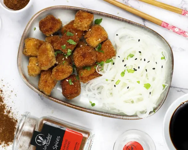 Chrupiące tofu w tempurze z makaronem ryżowym, posypane sezamem i szczypiorkiem. Obok sos sojowy i przyprawy.