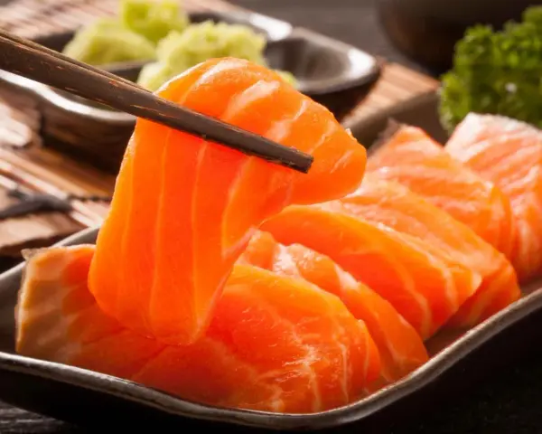 Sashimi co to? Świeży łosoś, chwytany pałeczkami, podany z wasabi i natką pietruszki.