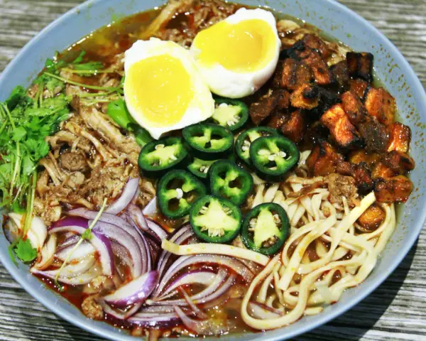 A miseczce ramen z wieprzowiną, jajkiem na pół, papryczkami jalapeño, cebulą i kolendrą.