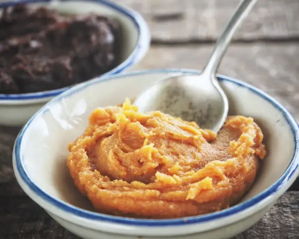 Pomarańczowa pasta miso w miseczce, obok ciemniejsza pasta. Łyżeczka zanurzona w jasnej paście.