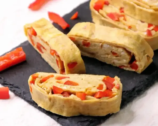Roladki z jajek z papryką, przypominające omlet do sushi, ułożone na czarnej desce.