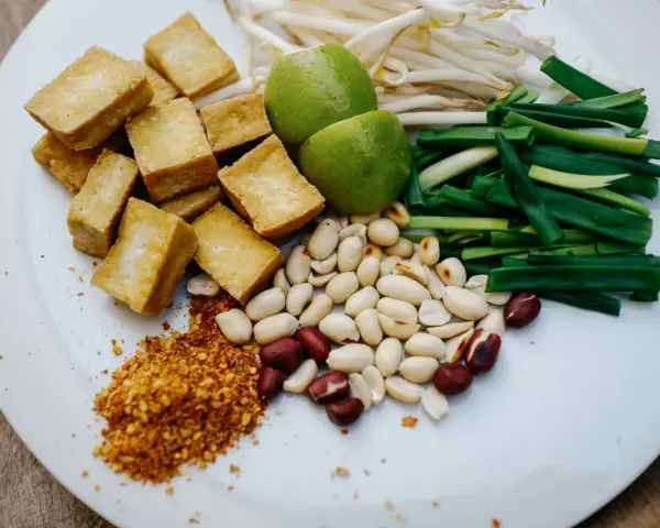 Na talerzu składniki do pad thai: smażone tofu, orzeszki ziemne, szczypiorek, kiełki fasoli mung, limonki i płatki chili. Gotowy sos pad thai czeka!