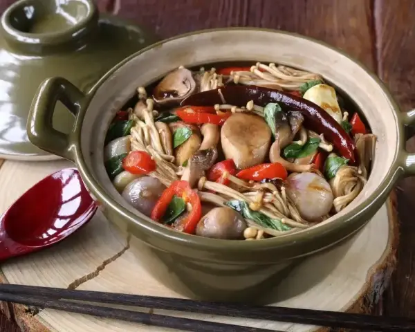 Gęsta zupa z grzybkami mun, enoki, pieczarkami, papryczkami chili i cebulką, podana w glinianym garnku.