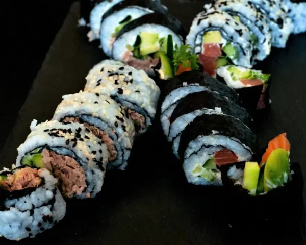 Pyszne rolki sushi z tuńczykiem i awokado, posypane sezamem. Idealna rzepa do sushi na czarnej desce.