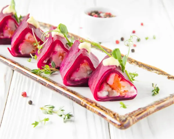 Roladki z buraka z farszem, przypominające sushi ze śledziem, ozdobione majonezem i ziołami.