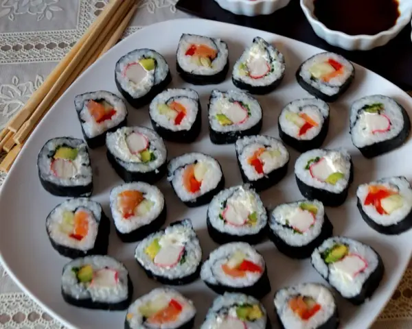 Talerz pełen sushi, w tym futomaki tamago z łososiem, awokado i paluszkami krabowymi.