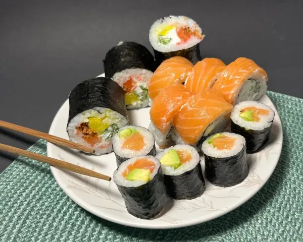 Talerz pełen sushi z łososiem i awokado. Wśród nich rolka z kremowym serkiem do sushi, idealna na przekąskę.