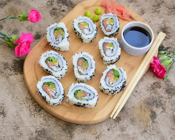 Pyszne california sushi z łososiem i awokado, posypane czarnym sezamem, podane z sosem sojowym i wasabi.