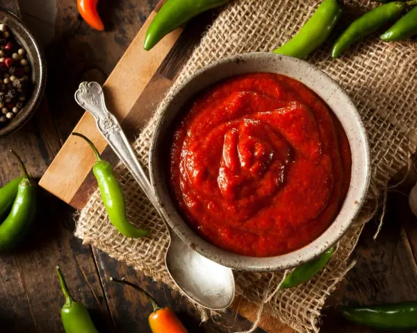 Miseczka z ostrym, czerwonym sosem, otoczona papryczkami chili, czosnkiem i pieprzem. Sriracha co to? To właśnie ten pikantny dodatek!