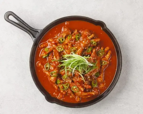 Kurczak w sosie gochujang, z zieloną cebulką i sezamem, podany na patelni.