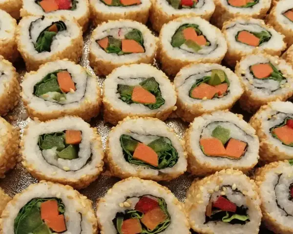 Roladki sushi z sezamem, w środku zielona sałata i pomarańczowa marchewka do sushi.