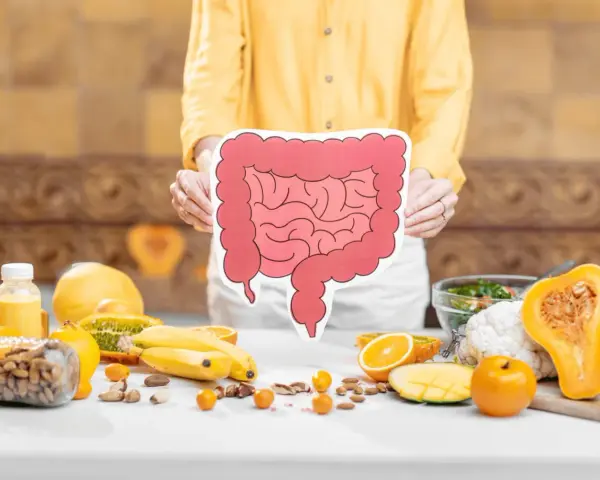Osoba trzyma planszę z jelitami, wokół owoce i orzechy. Czy sos sojowy fodmap jest bezpieczny?