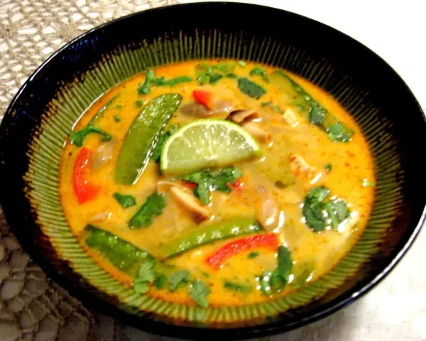 Aksamitna zupa tom kha z kurczakiem, z zielonym groszkiem, papryką i plasterkiem limonki.
