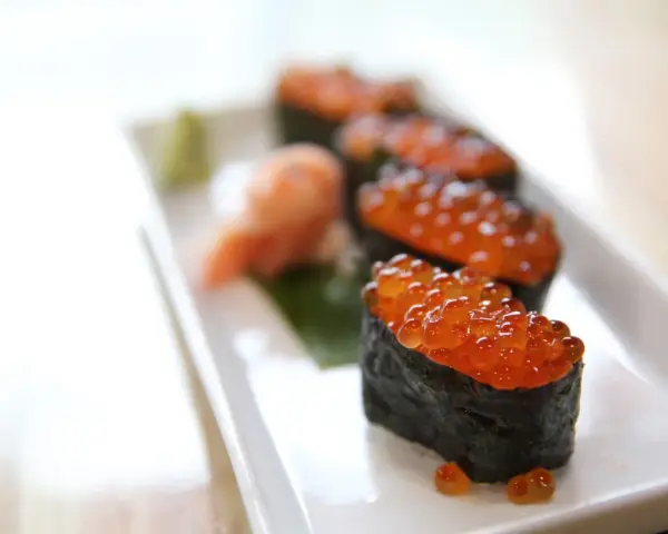 Pięć kawałków sushi z kawiorem, podanych na białym talerzu z odrobiną wasabi i marynowanego imbiru.