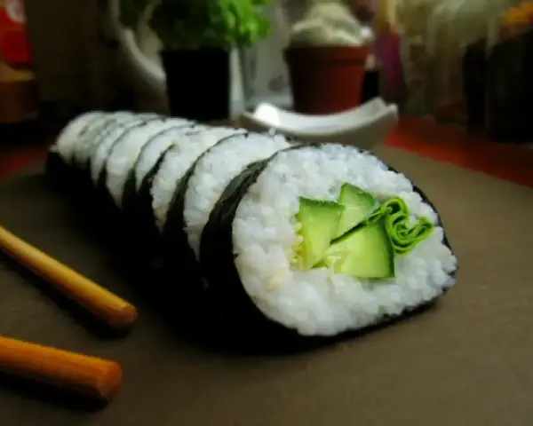 Świeży ogórek do sushi, zwinięty w rolkę z ryżem i nori. Obok leżą pałeczki.