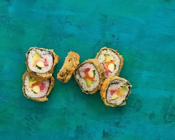 Chrupiące sushi w panierce z łososiem, awokado i ogórkiem na turkusowym tle.