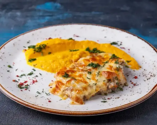 Pyszny katsu z kurczaka zapieczony z serem, podany z purée z dyni i posypany ziołami.