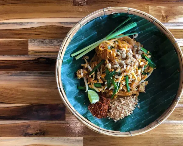 Pyszne pad thai skladniki: makaron ryżowy, kiełki, szczypiorek, orzeszki ziemne, chili i limonka na liściu bananowca.