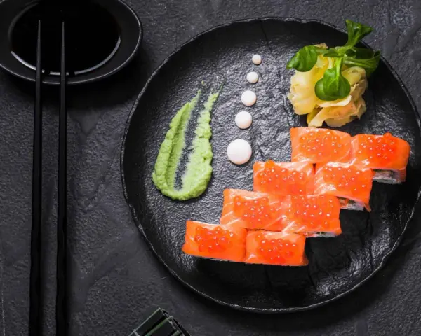 Roladki sushi z łososiem i ikrą, podane z zielonym, pikantnym wasabi prawdziwe, imbirem i sosem sojowym.