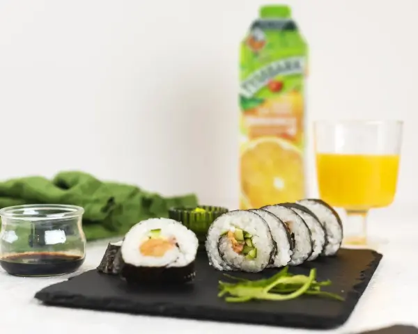 Roladki sushi z surowym łososiem do sushi, ogórkiem i ryżem, podane z sosem sojowym i sokiem pomarańczowym.