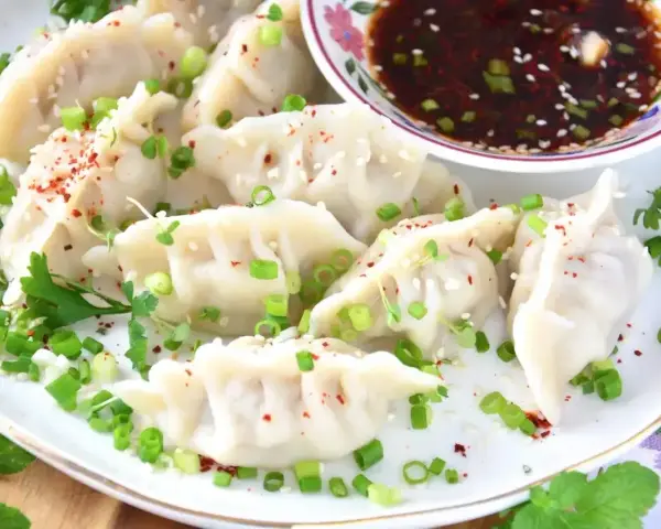 Pyszne pierożki gyoza posypane szczypiorkiem i sezamem, podane z aromatycznym sosem.