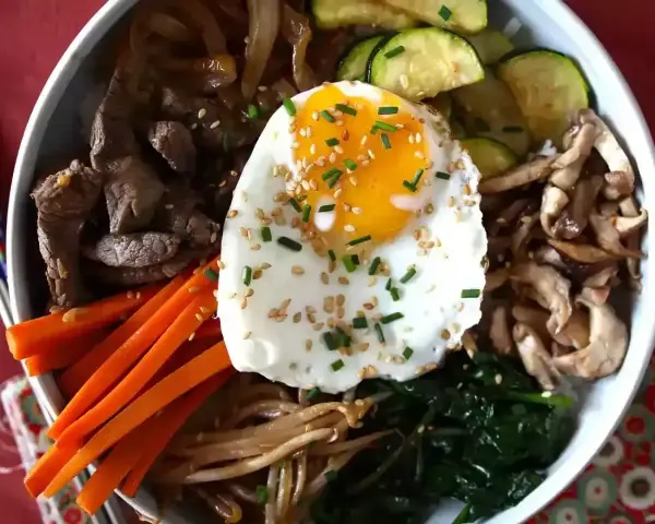 Apetyczne koreańskie dania: bibimbap z wołowiną, warzywami, grzybami i jajkiem sadzonym, posypane sezamem i szczypiorkiem.