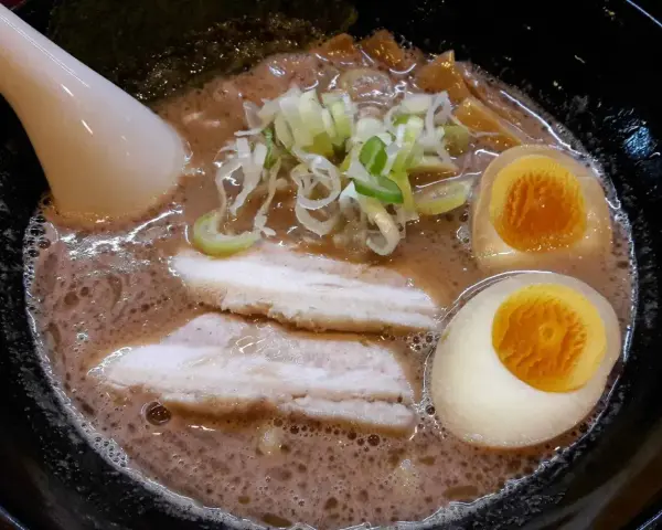 Aksamitny bulion, dwa połówki jajka na miękko, plastry boczku i szczypiorek tworzą apetyczny ramen z boczkiem.