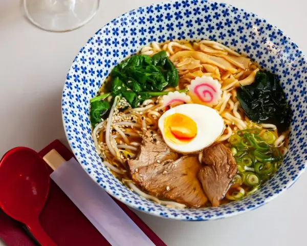 Miseczka aromatycznego makaronu ramen z jajkiem, mięsem, warzywami i kiełkami. Idealny posiłek, który dostarczy energii i zaspokoi głód.