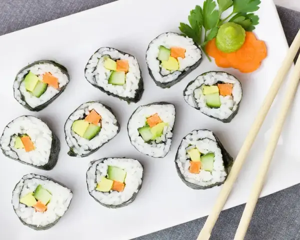 Talerz z hosomaki awokado, ogórkiem i marchewką, udekorowany wasabi i natką pietruszki.