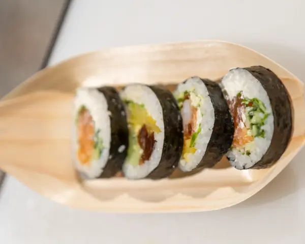 Pięć kawałków sushi z łososiem, awokado i krewetkami na drewnianej łódce. Różne rodzaje sushi nazwy.