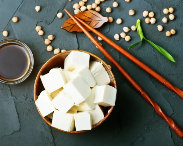 Kostki tofu, czyli przetworzona fasola sojowa, w drewnianej misce, obok sosu sojowego i pałeczek.