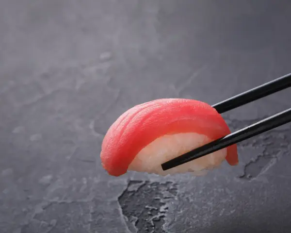 Pałeczki trzymają kawałek sushi z tuńczykiem. Czy sushi jest dobre? Wygląda apetycznie!