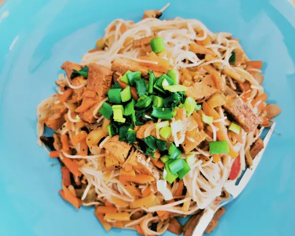 Pyszne tofu po chińsku z makaronem ryżowym, warzywami i szczypiorkiem na niebieskim talerzu.