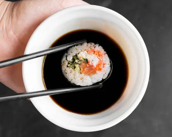 Pałeczkami zanurzam sushi z łososiem i kremowym nadzieniem w sosie sojowym. Idealny sojowy ser do sushi.