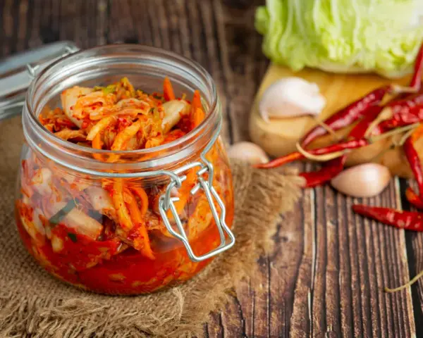 Słoik z kimchi na tle desek, z suszonymi papryczkami chili i czosnkiem.