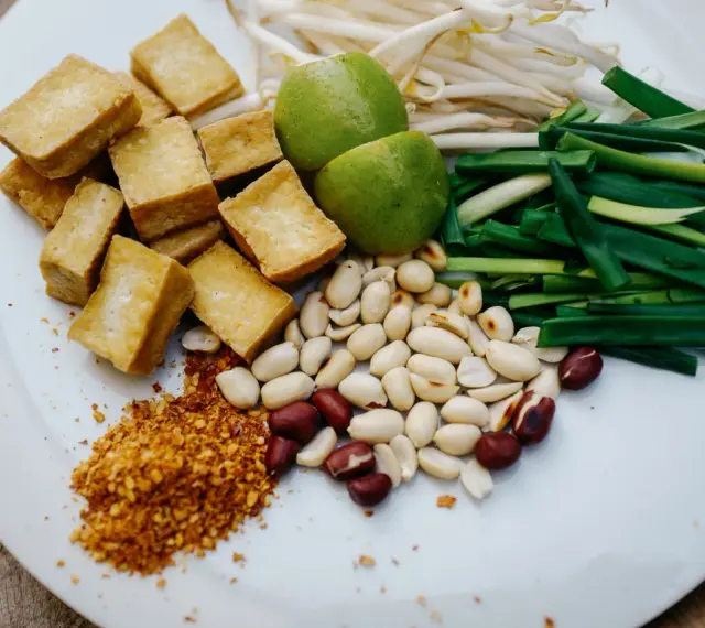Na talerzu składniki do pad thai: smażone tofu, orzeszki ziemne, szczypiorek, kiełki fasoli mung, limonki i płatki chili. Gotowy sos pad thai czeka!