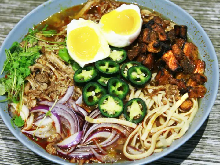 A miseczce ramen z wieprzowiną, jajkiem na pół, papryczkami jalapeño, cebulą i kolendrą.