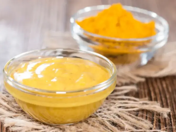 Dwie szklane miseczki na drewnianym tle. Jedna zawiera gładki sos, druga żółtą przyprawę, składniki do korma curry.