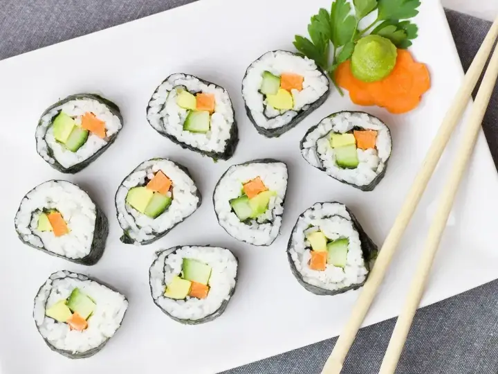 Talerz z hosomaki awokado, ogórkiem i marchewką, udekorowany wasabi i natką pietruszki.