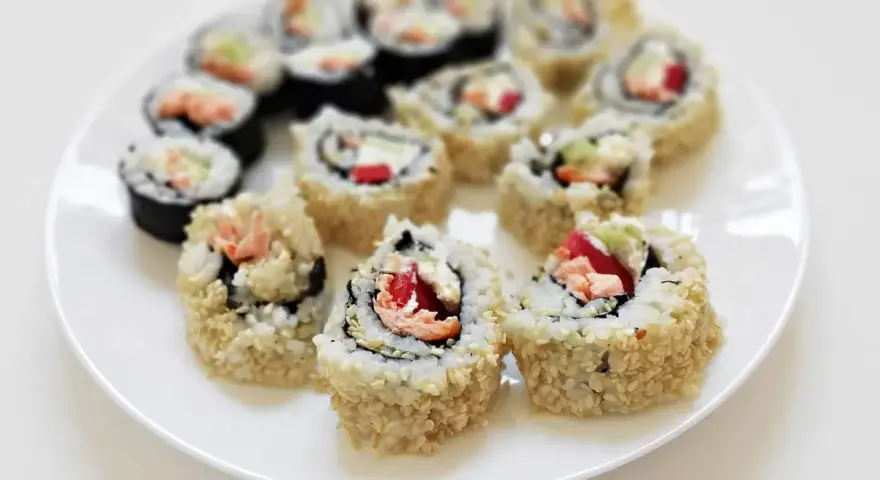 Talerz sushi z hosomaki takuan, łososiem i warzywami. Roladki ryżowe w sezamie i nori.
